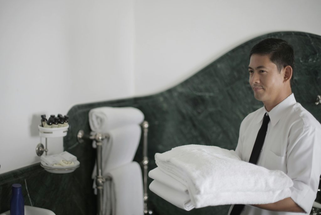pexels photo 3770238 3770238 Side view of smiling ethnic male hotel employee holding stack of clean white towels while cleaning bathroom